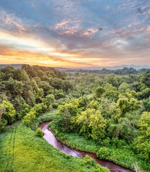 Stunning aerial view of a lush forest and winding creek in Misha Mokwa, WI, during a colorful sunset.