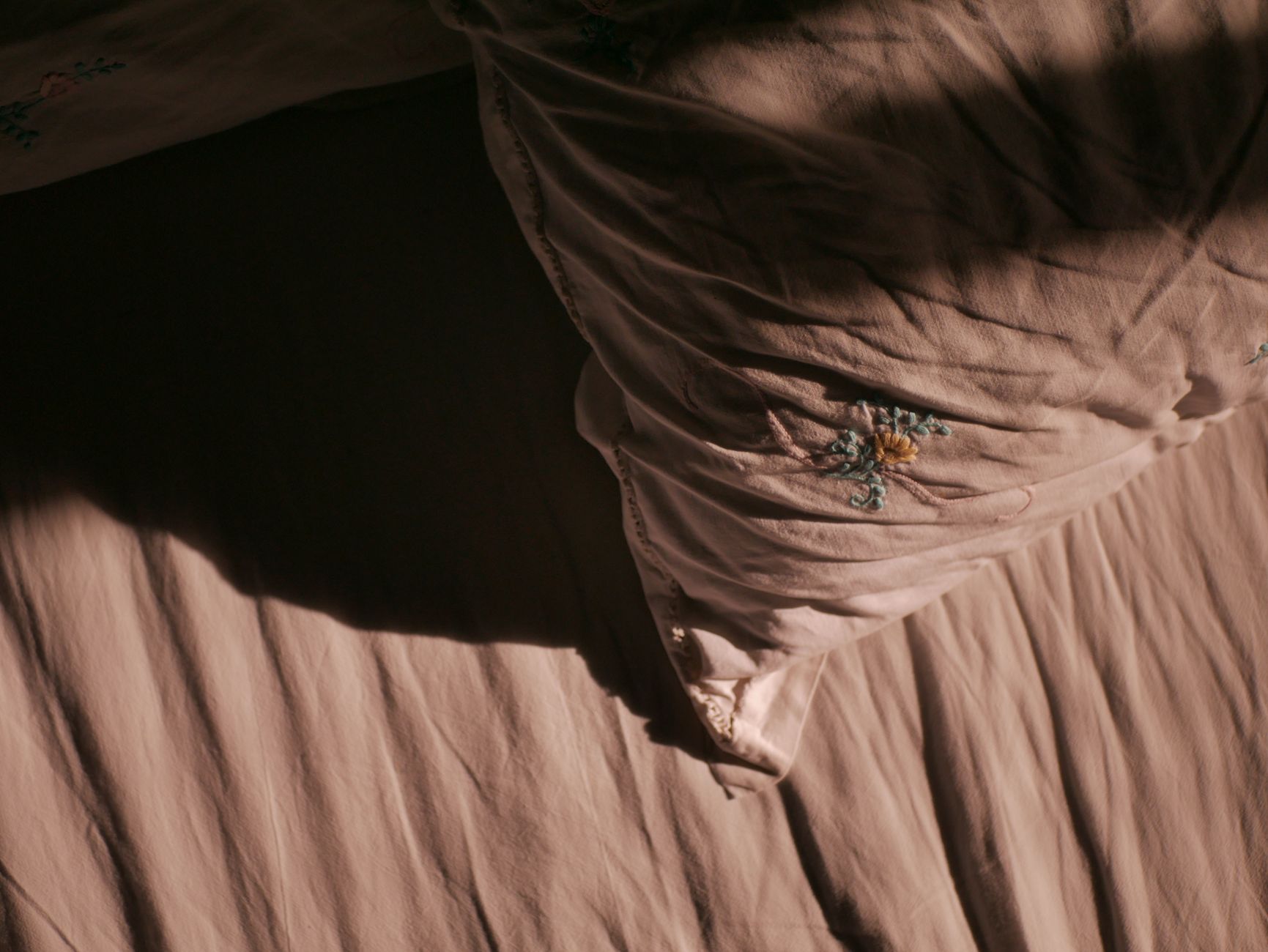 A minimalist photo of a floral embroidered pillow with warm shadows on a bed.