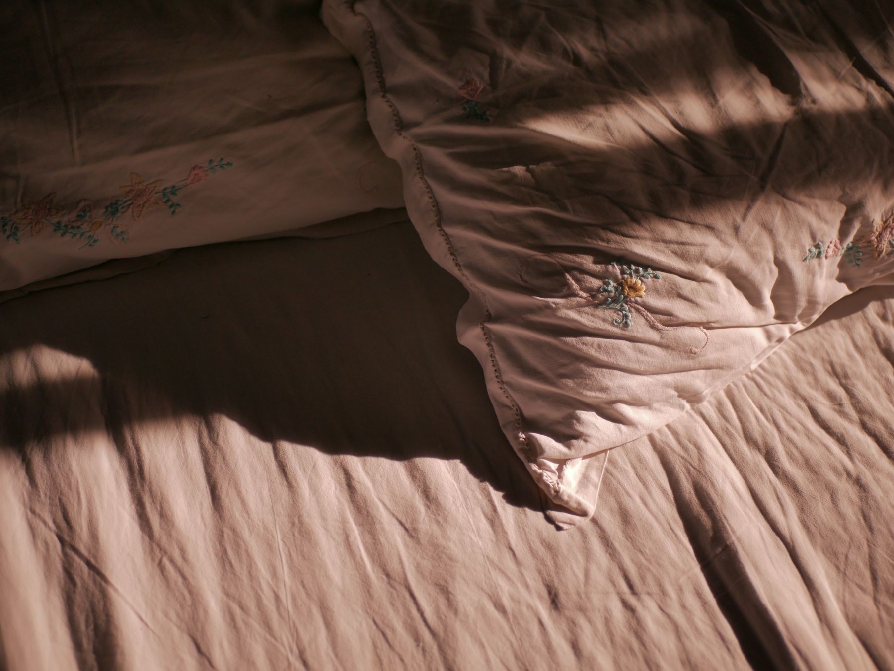 Soft light falling across rose-colored bedding on a made bed