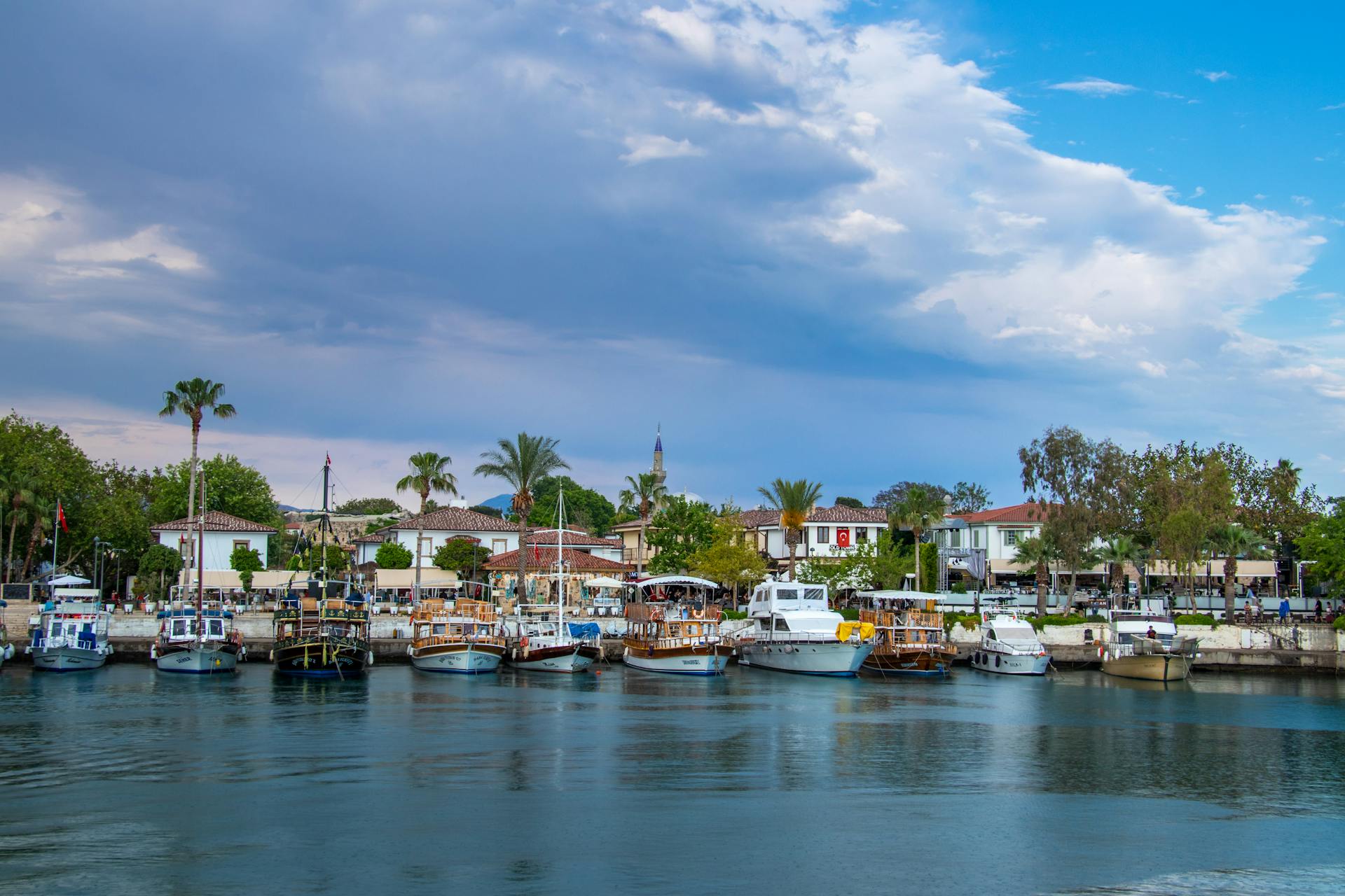 Boats docked at a picturesque harbor with palm trees under a blue sky.