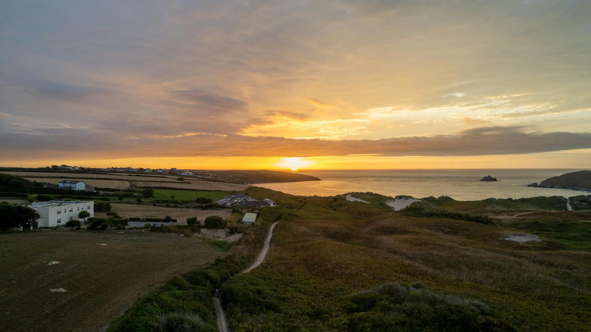 Scenic sunset view over Cornwall's lush countryside and coastline, capturing serene beauty.