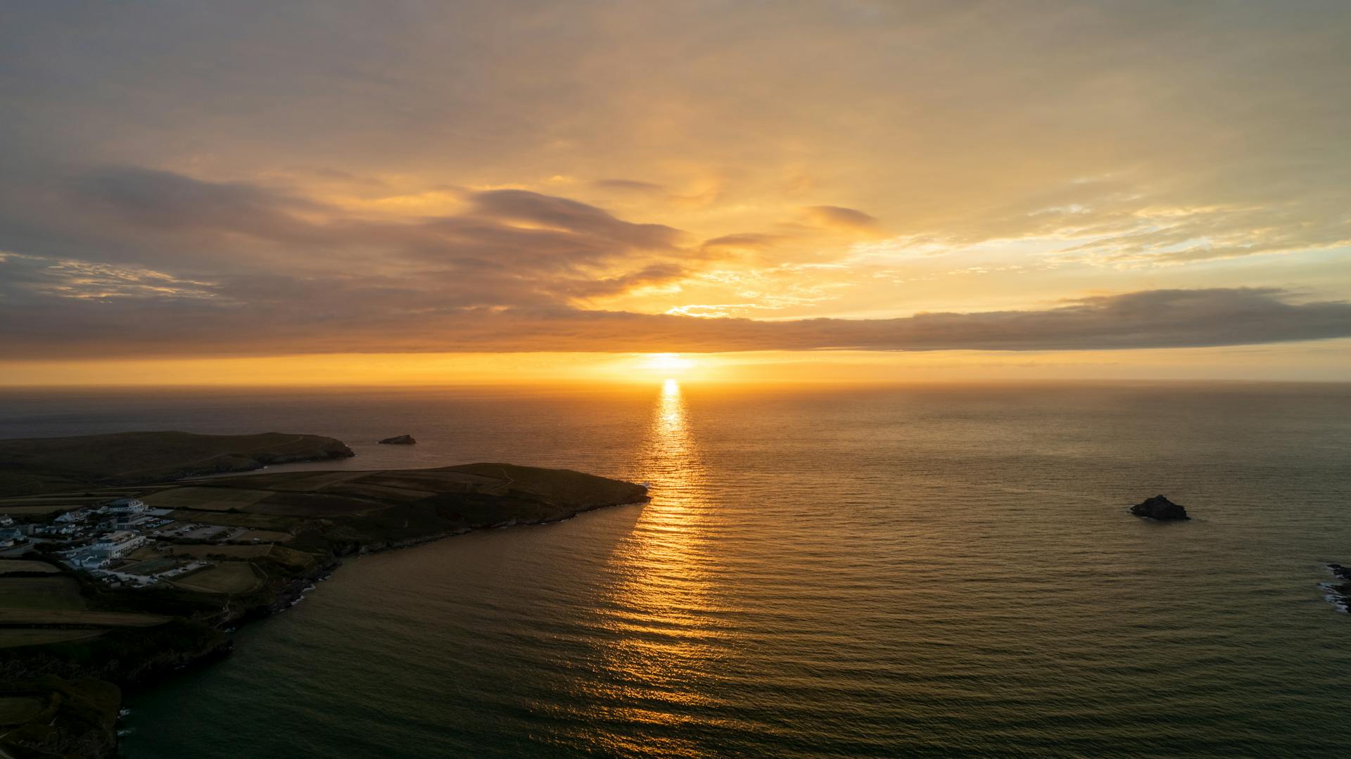 A breathtaking sunset view along the Cornwall coastline with a vibrant sky reflecting on the ocean.
