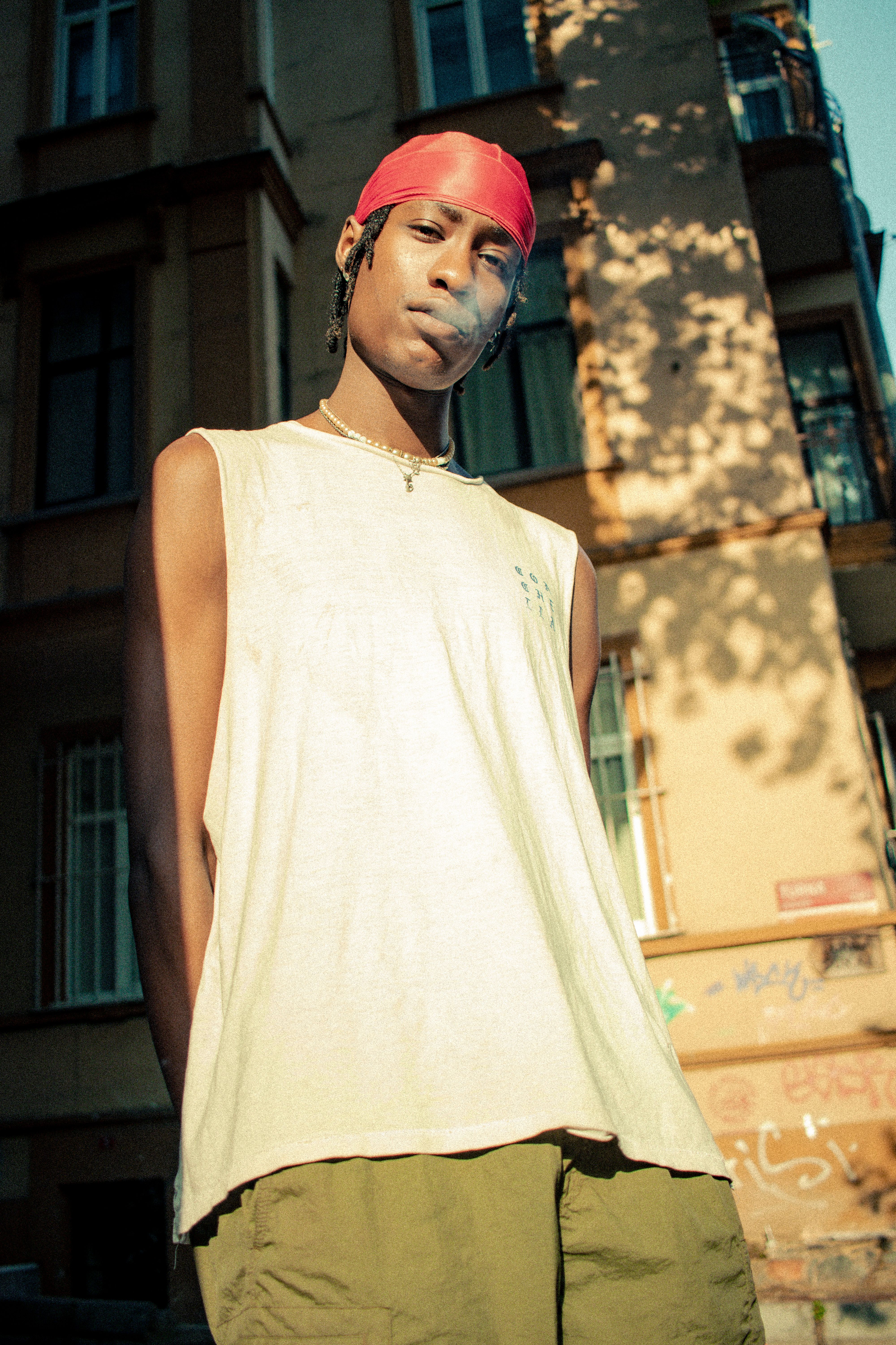 A young man smokes in front of an urban building, casting a stylish pose.