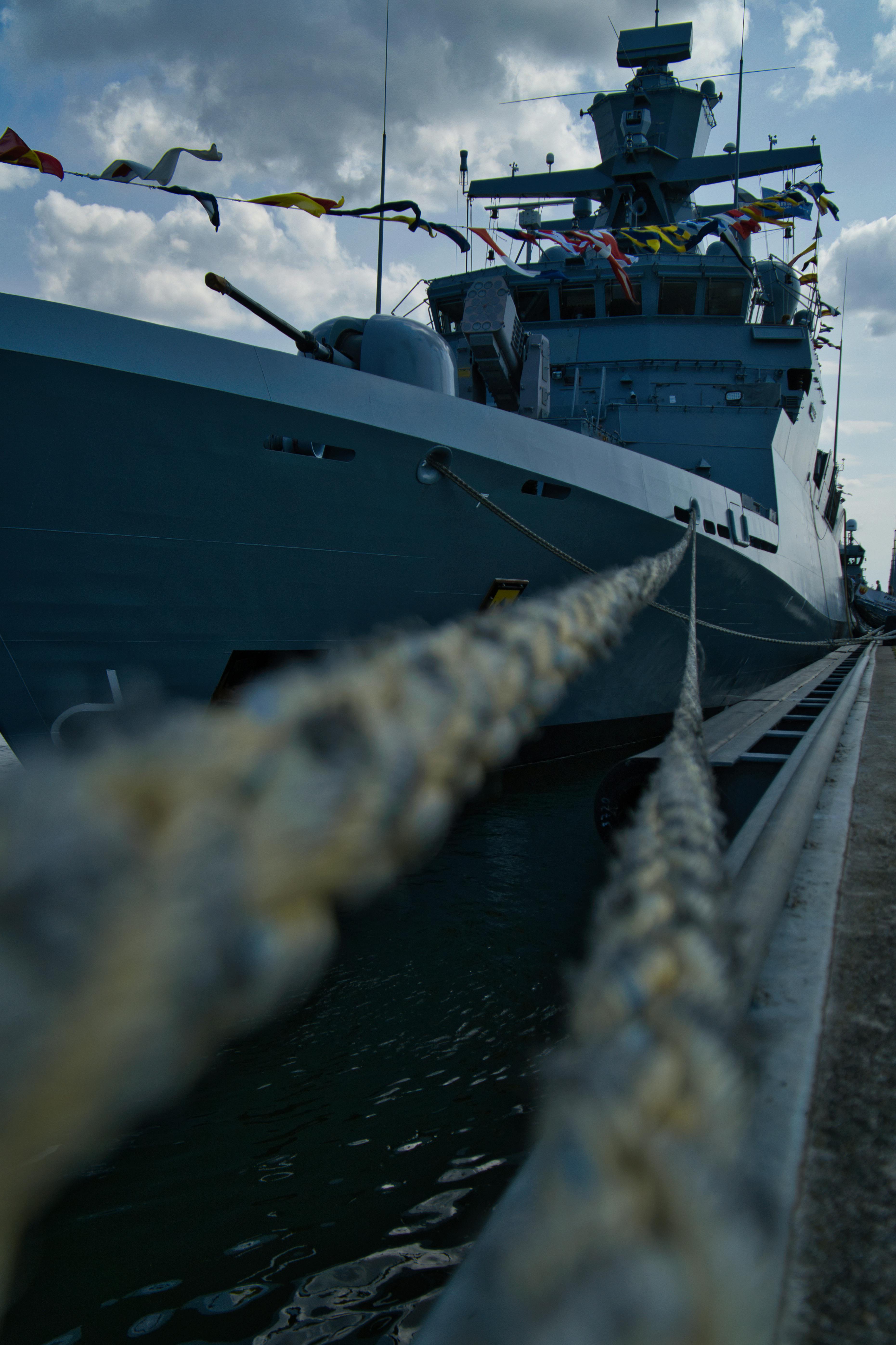 A navy warship docked at Rostock harbor, showcasing its impressive structure and colorful flags.