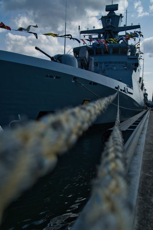 Free A navy warship docked at Rostock harbor, showcasing its impressive structure and colorful flags. Stock Photo