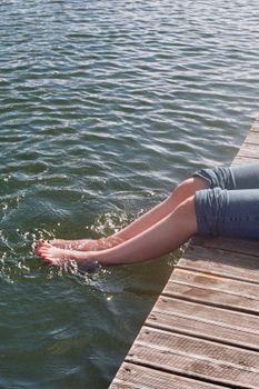 A woman dips her legs in the lake, enjoying a sunny summer day by the water.