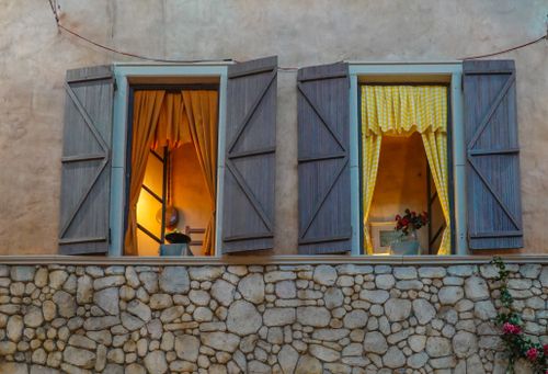 Free Evening view of a stone facade with illuminated windows and rustic shutters. Stock Photo