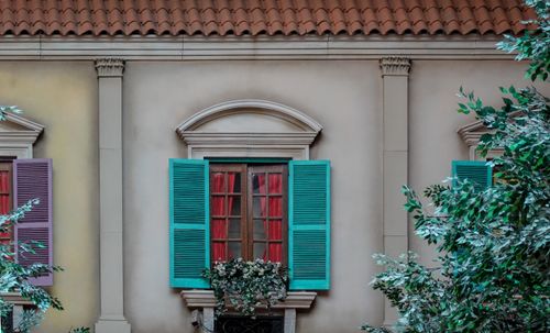 Free Mediterranean-style window with colorful shutters and greenery, conveying rustic charm. Stock Photo