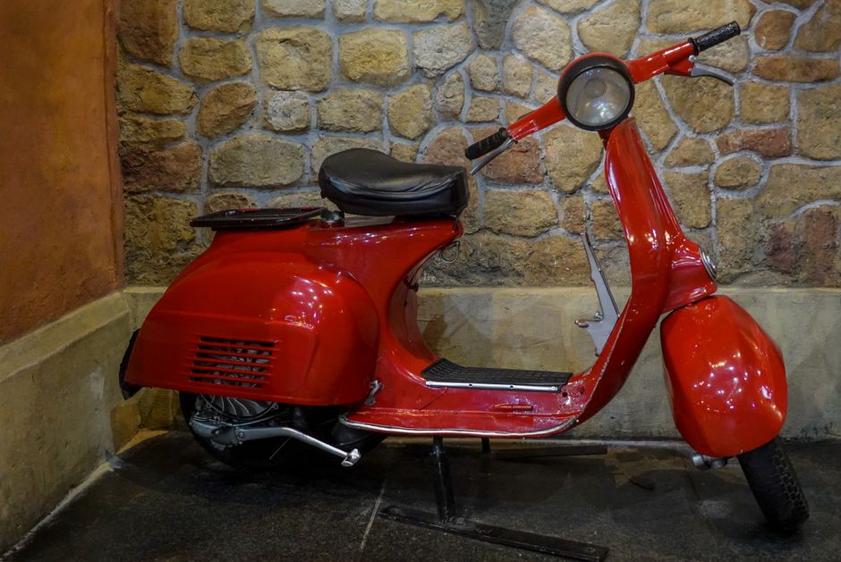 Classic red vintage Vespa scooter parked against a rustic stone wall indoors.