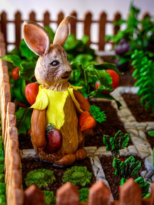 Free Adorable rabbit sculpture holding vegetables in a vibrant garden. Perfect for whimsical and nature-themed decor. Stock Photo