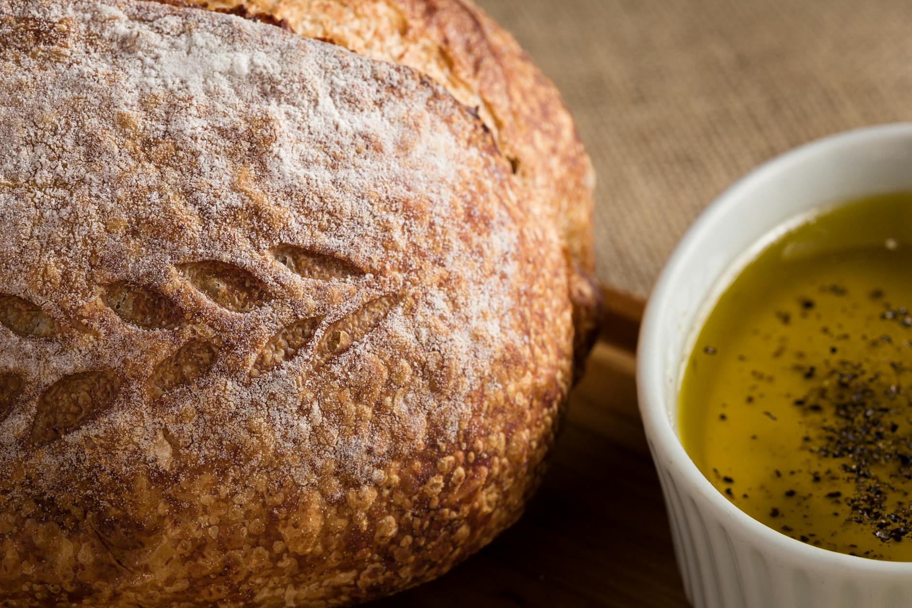 Close-up of a rustic loaf of bread next to a bowl of olive oil seasoned with pepper.