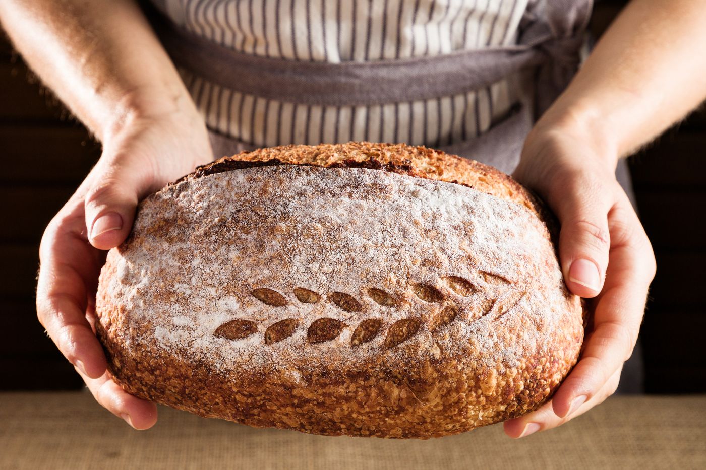 Hands holding a freshly baked, leaf-scored sourdough loaf