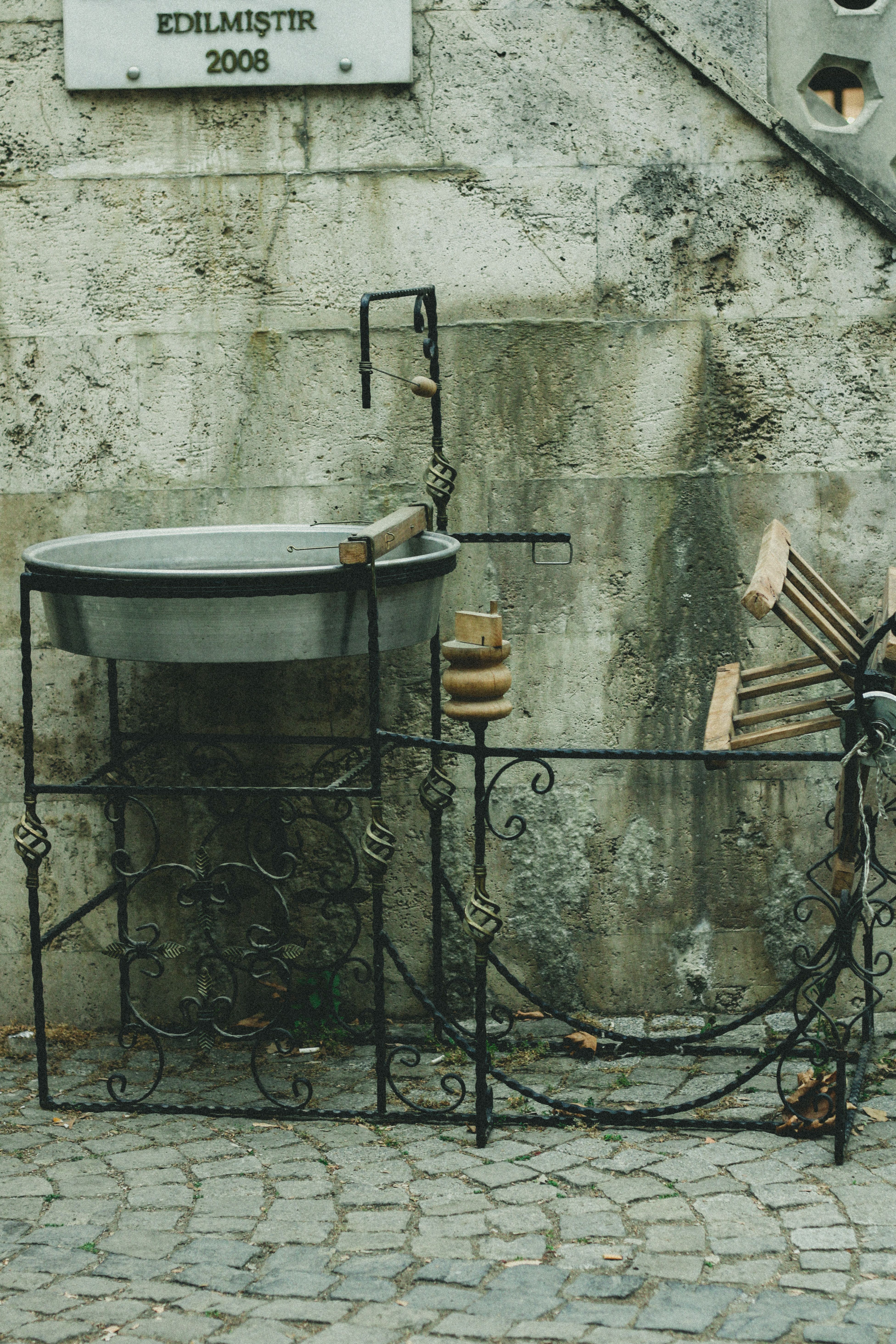 A vintage-style metal basin setup in an urban cobblestone street with stone wall backdrop.