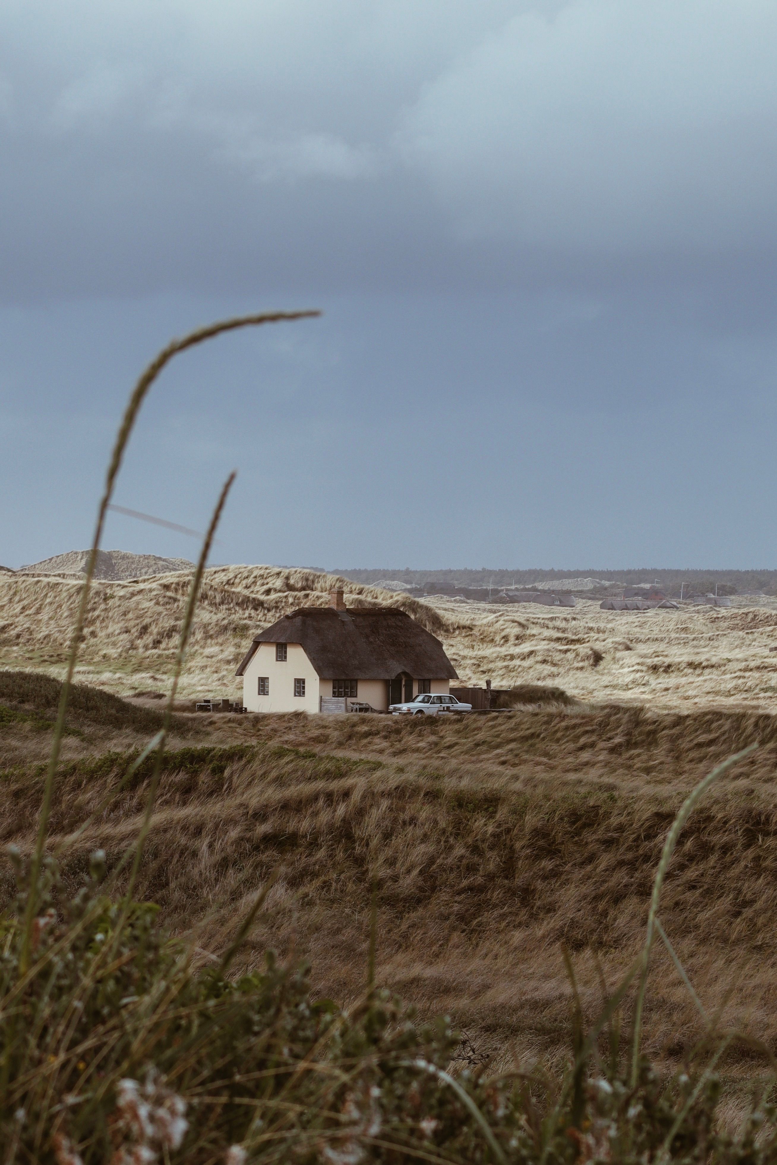 A picturesque Danish cottage set against a serene rural landscape under a cloudy sky.