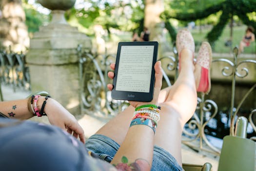 A woman leisurely reading a Kobo e-reader outdoors with colorful bracelets and a tattoo visible.