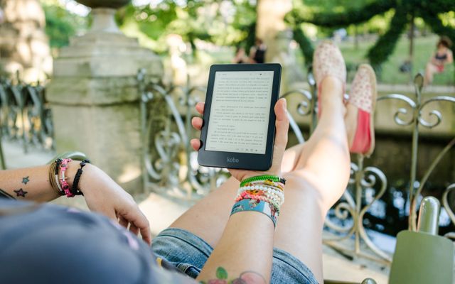 A woman reading on a Kobo e-reader in a sunny park