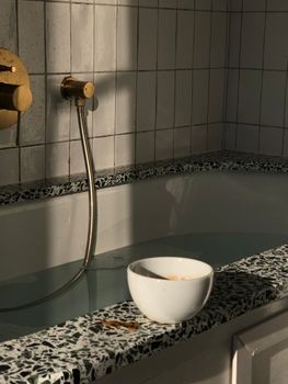 Elegant bathroom with terrazzo tub edge and ceramic cup in soft lighting, Paris.