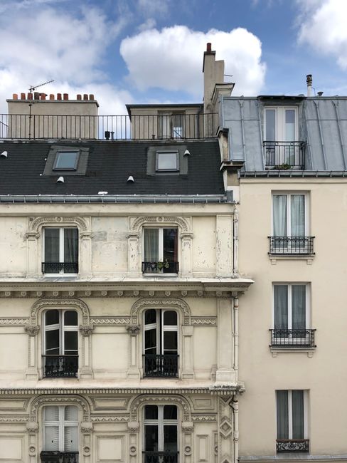 Classic Parisian apartment buildings with ornate facades and rooftop details under a blue sky.