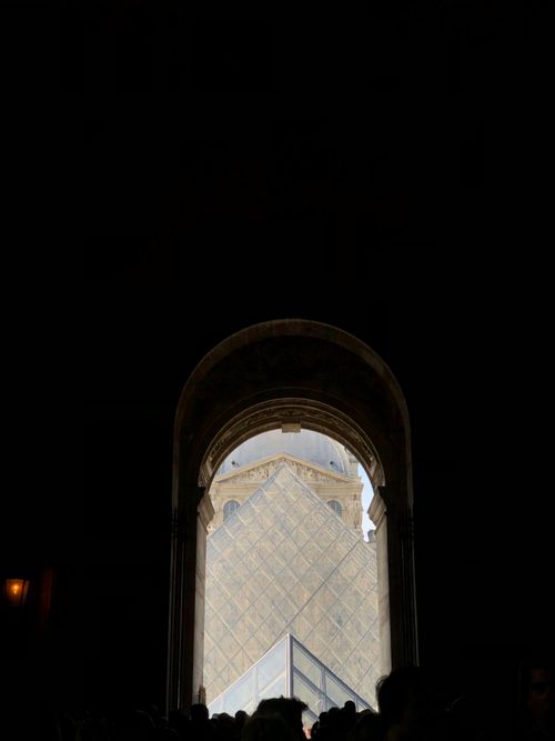 Free A striking view of the Louvre Pyramid framed by a dark archway entrance. Stock Photo
