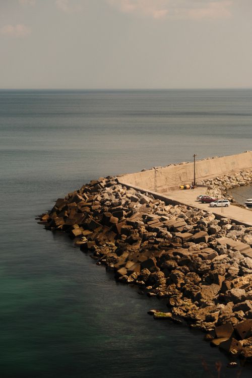 Free Aerial view of rocky embankment by the ocean with parked cars on a sunny day. Stock Photo