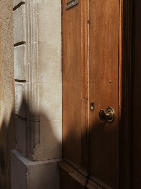 Close-up of a wooden door with brass knob, casting shadows on stone facade.