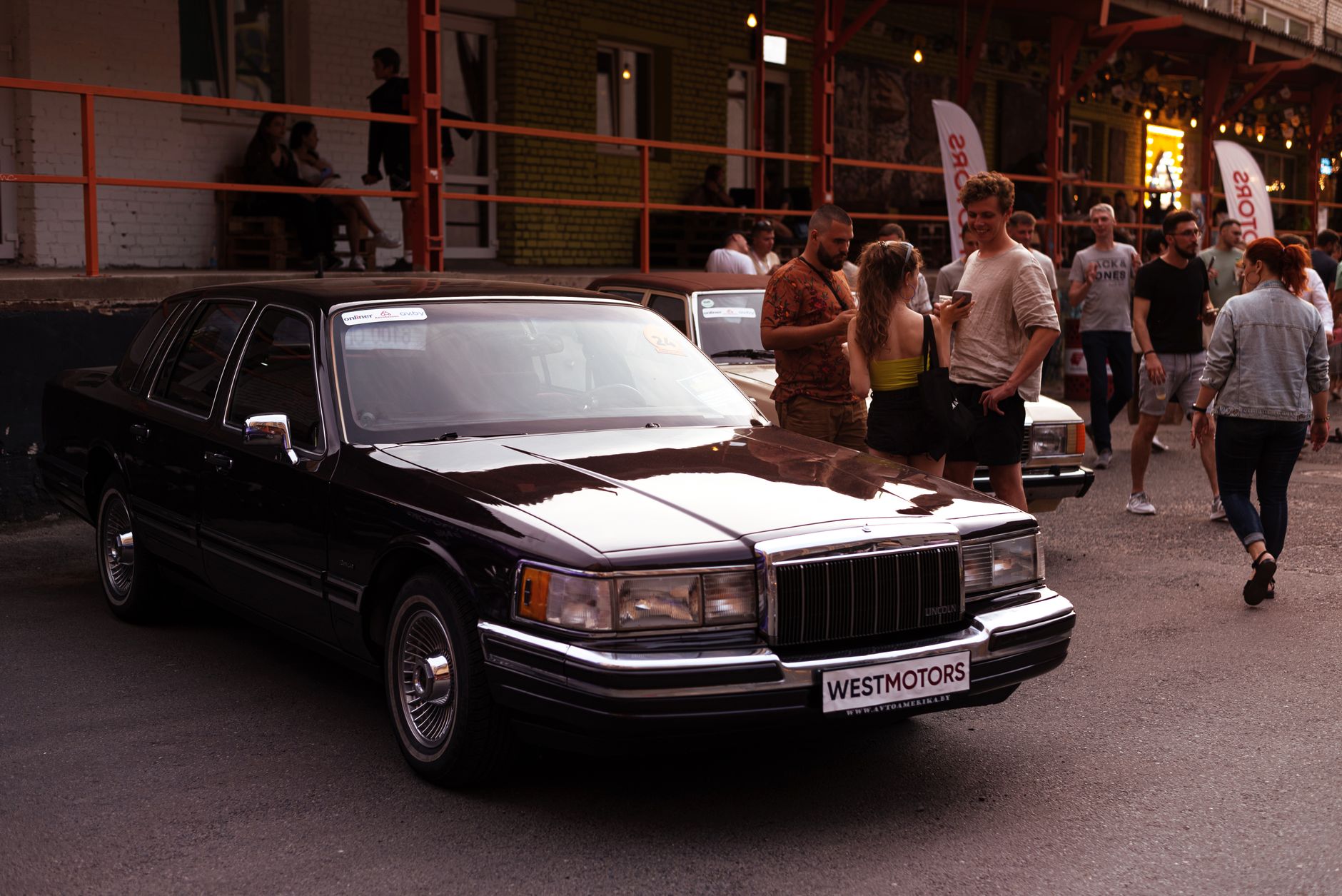 Vintage Lincoln Town Car displayed at an outdoor automotive event with people socializing nearby.