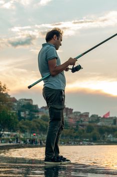 Man casting a fishing rod by the Bosphorus in Istanbul during sunset, enjoying leisure time.