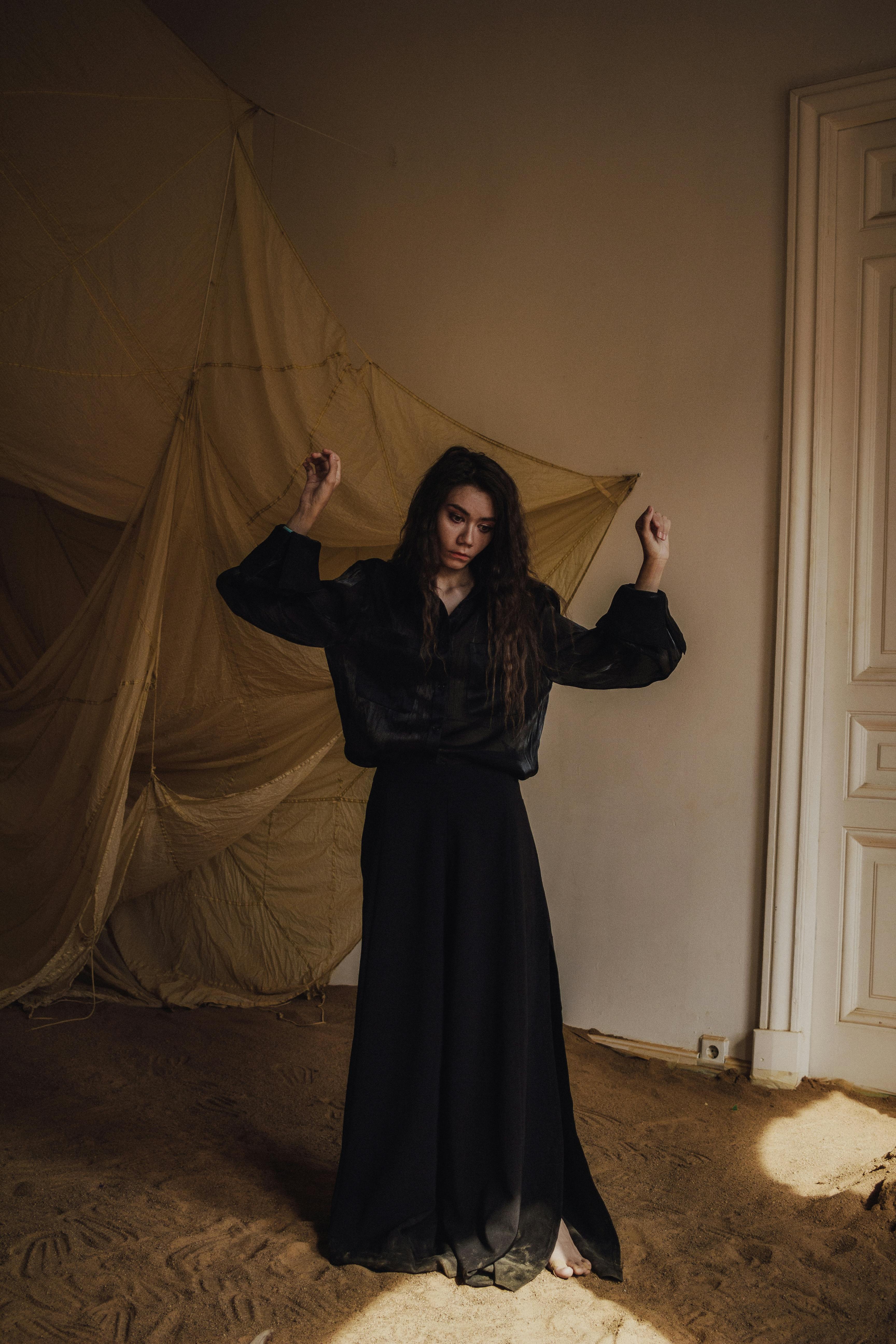 Portrait of a woman in a flowing black dress posing elegantly against a draped fabric backdrop.