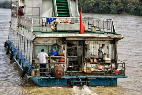 Free Ferry boat with workers cooking on a river, showcasing transportation and livelihood. Stock Photo