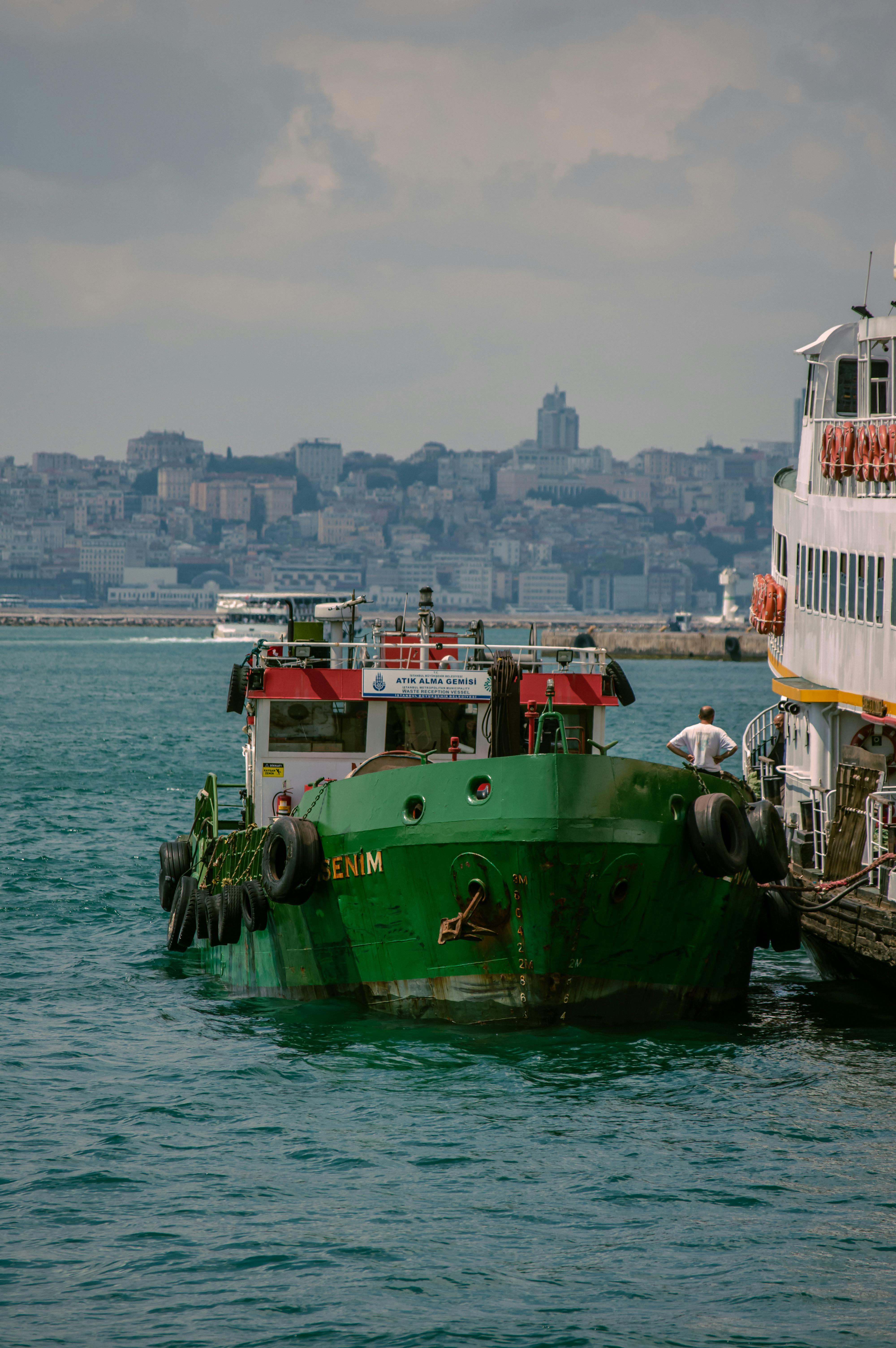 Free Green cargo boat docked in Istanbul with cityscape in the background. Stock Photo