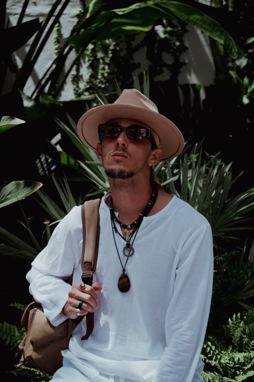 Free Stylish man wearing white clothes and sunglasses, carrying a backpack in tropical greenery. Stock Photo