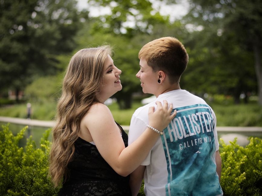 A young couple smiling and embracing outdoors in a green park setting during the day.