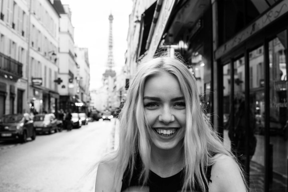 Black and white portrait of a smiling woman on a Paris street with the Eiffel Tower in the background.