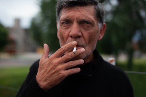 A Man in Black Sweater Smoking a Cigarette