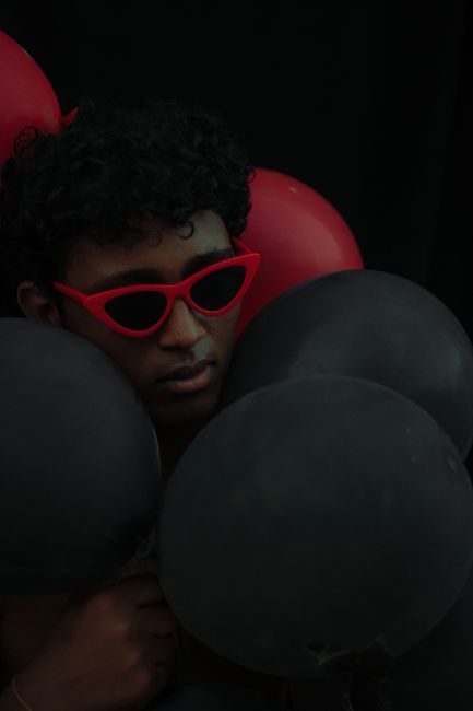 Stylish portrait of a man with red sunglasses holding black and red balloons.
