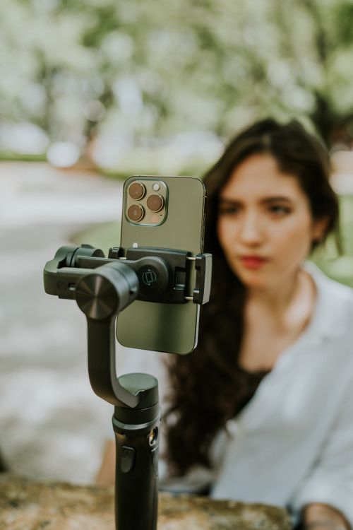 Free A woman using a gimbal-mounted smartphone for video recording outdoors, blurred background. Stock Photo