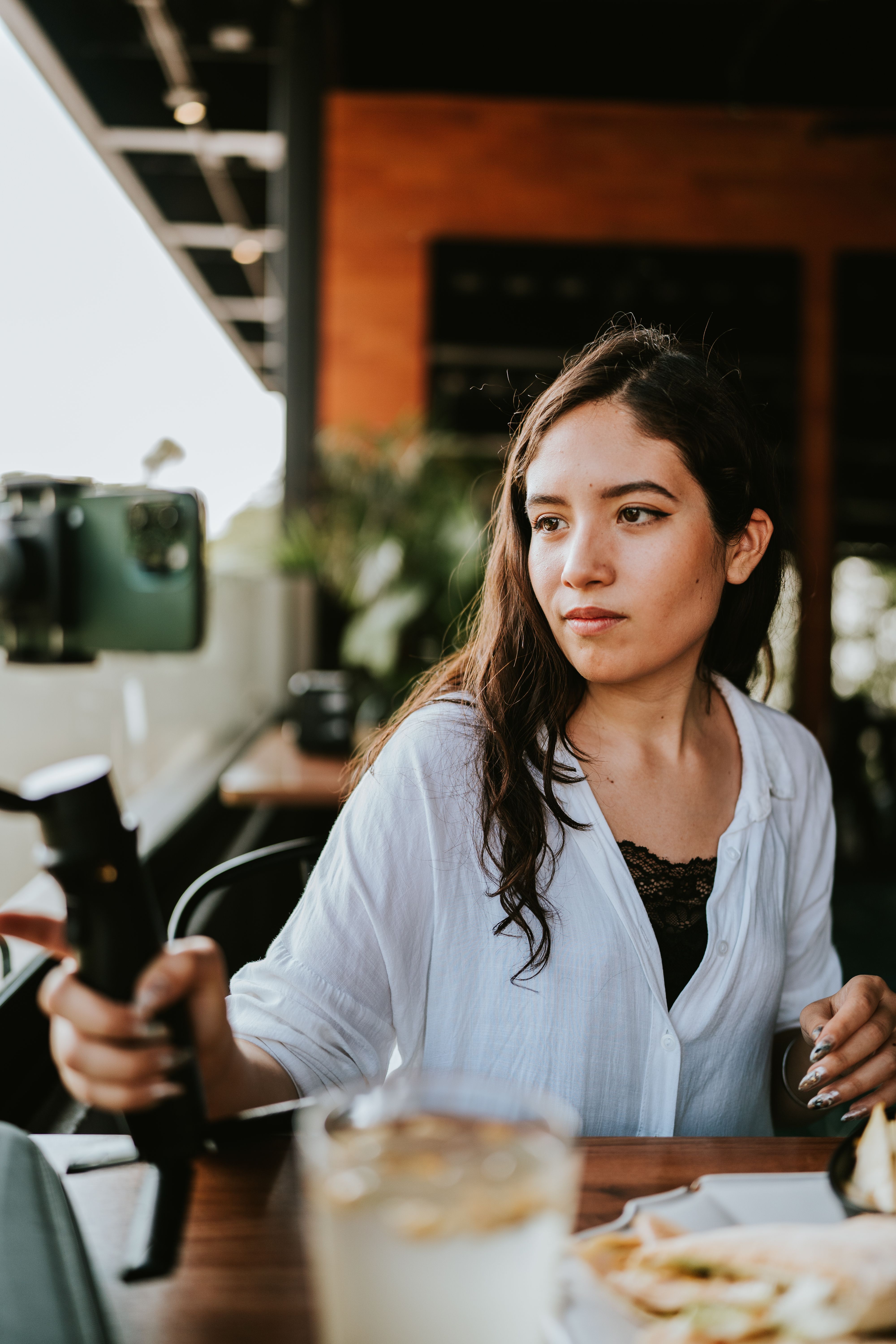 Young woman in a relaxed cafe setting taking a selfie with a smartphone on a tripod.
