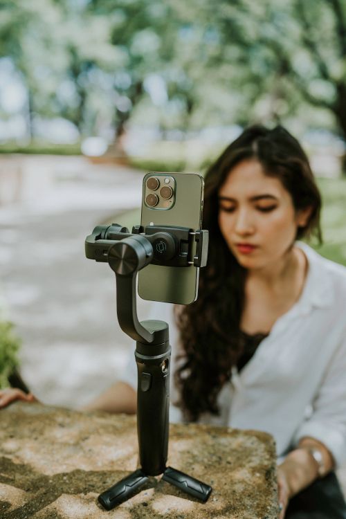 Free Woman interacts with smartphone on gimbal outdoors in sunlit setting. Stock Photo