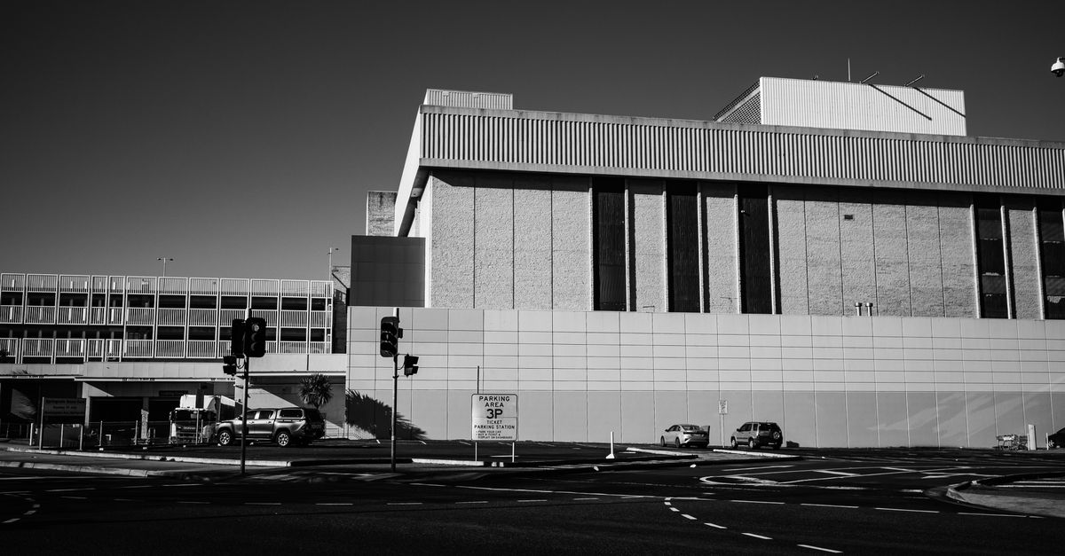 Grayscale Photo of a Road Intersection Beside a Building · Free Stock Photo