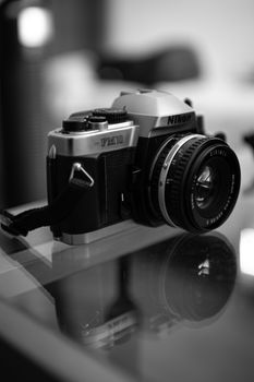 Black and white close-up of a vintage Nikon camera on a reflective surface.
