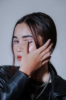 A fashionable young woman posing with hand on face wearing a black leather jacket.