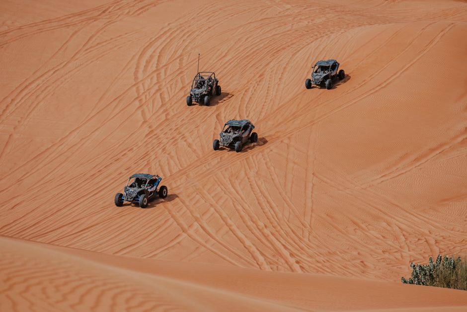 Four dune buggies driving in formation across desert sand dunes, showcasing adventure and thrill.