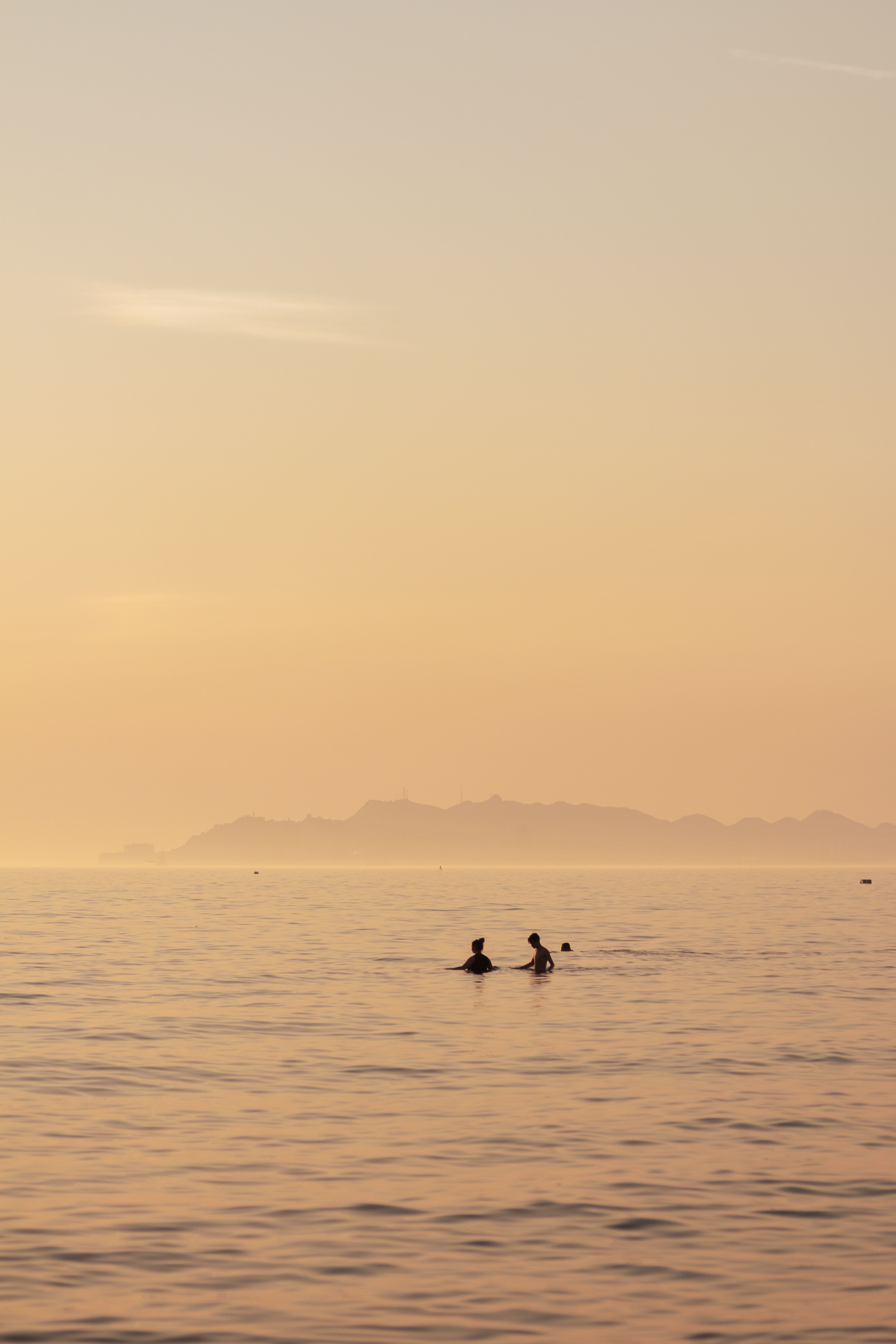 Capture of people swimming at sunset with an island view in Durrës, Albania.