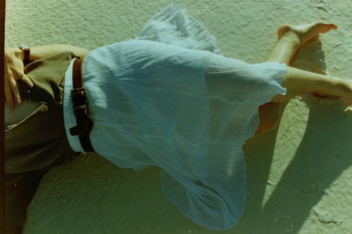 Free A woman lies barefoot on a sandy beach wearing a white skirt, captured in a vintage style. Stock Photo