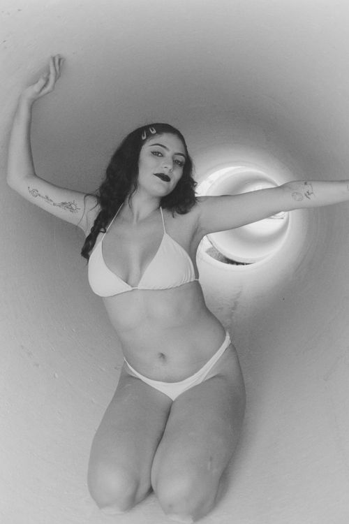 Free A striking black and white portrait of a woman kneeling in a tube, showcasing elegance and style. Stock Photo