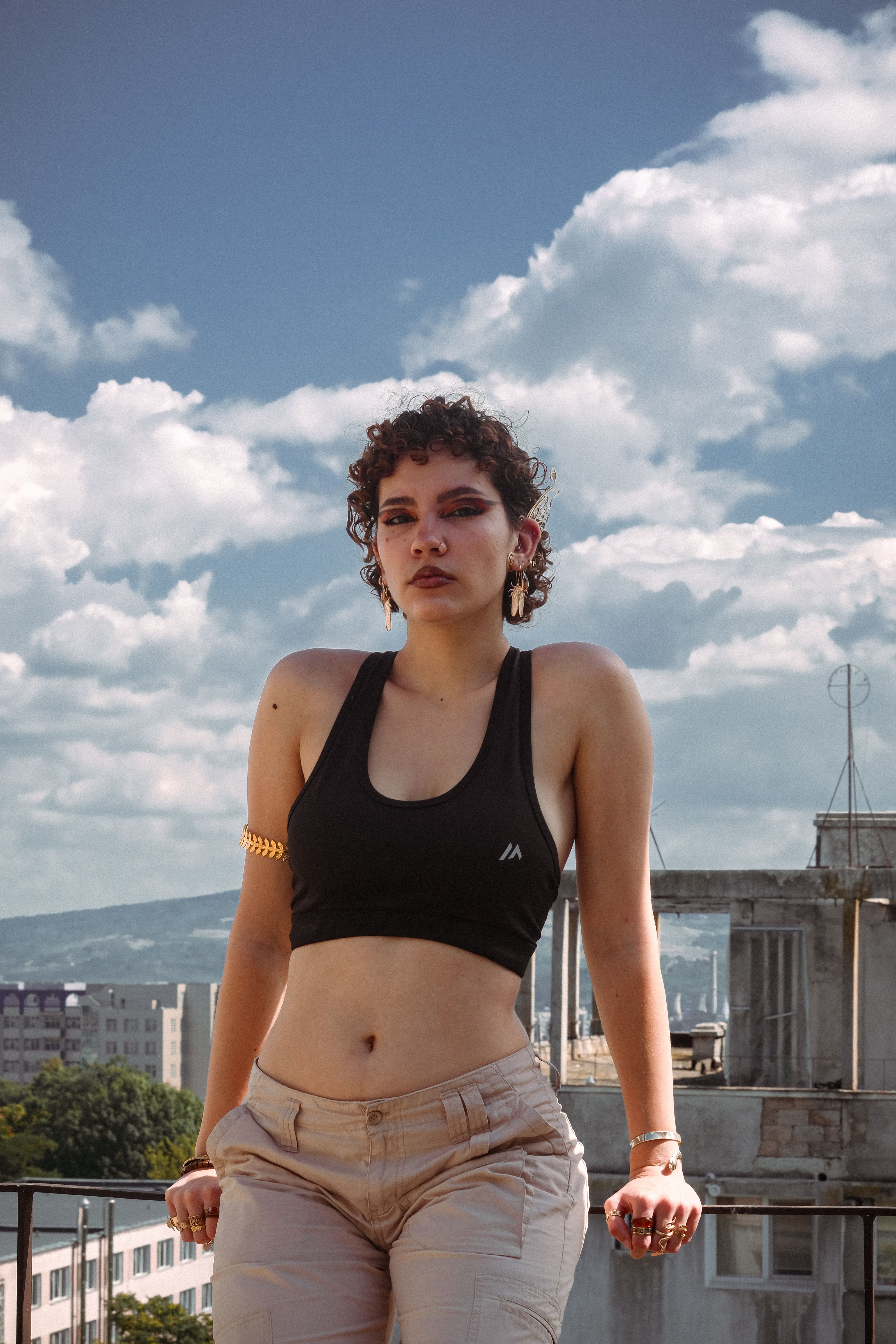 A stylish woman in athletic wear poses outdoors with a scenic city and sky background, exuding confidence.