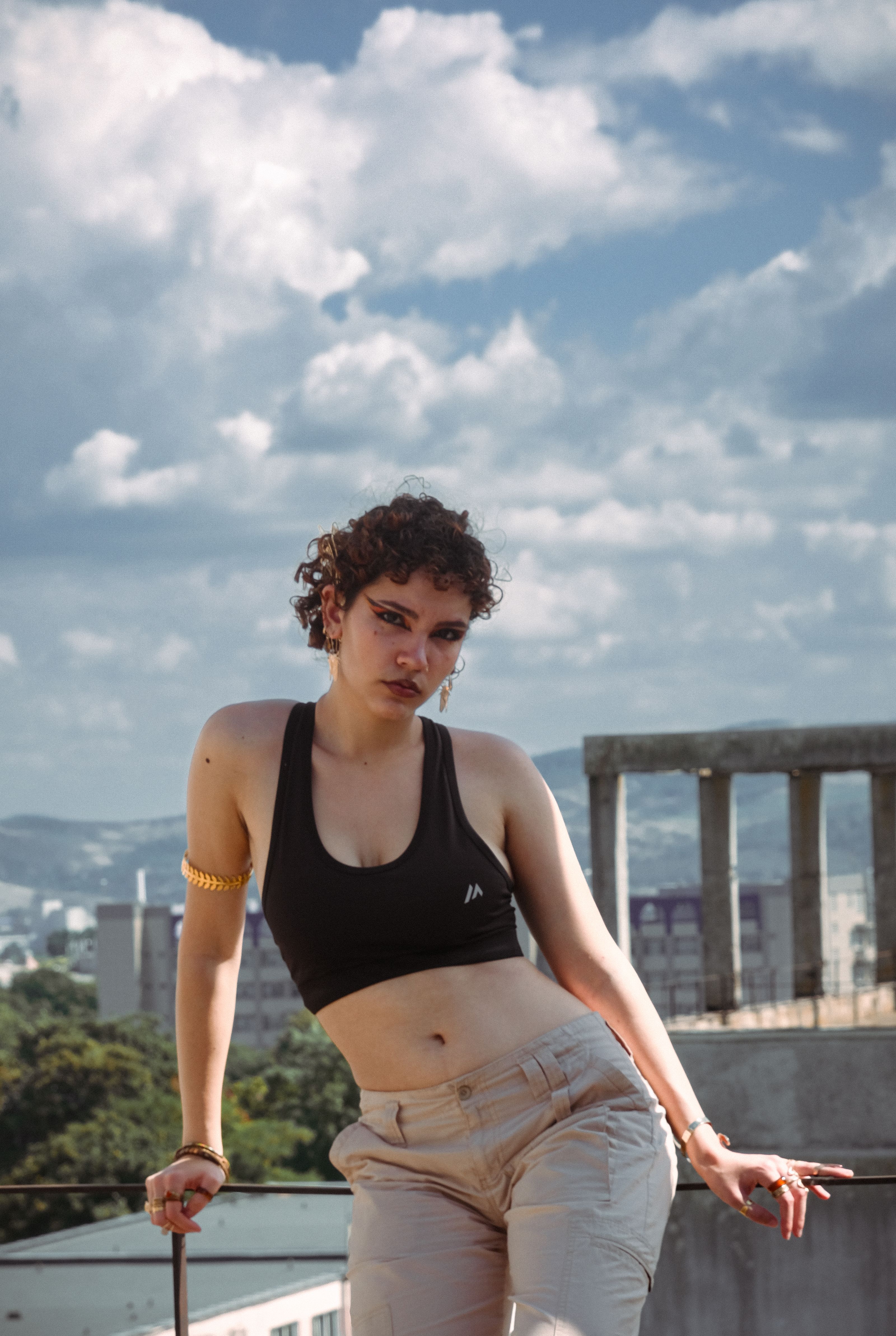 Mulher fashion com top cropped preto posando no telhado contra um céu azul brilhante.