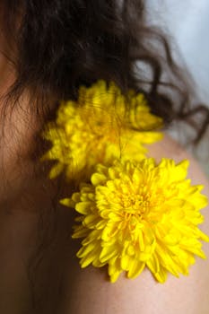 Bright yellow chrysanthemums on skin with curly hair, symbolizing natural beauty and floral elegance.