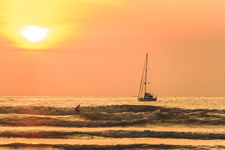 A Boat And A Person Surfing On Beach Waves