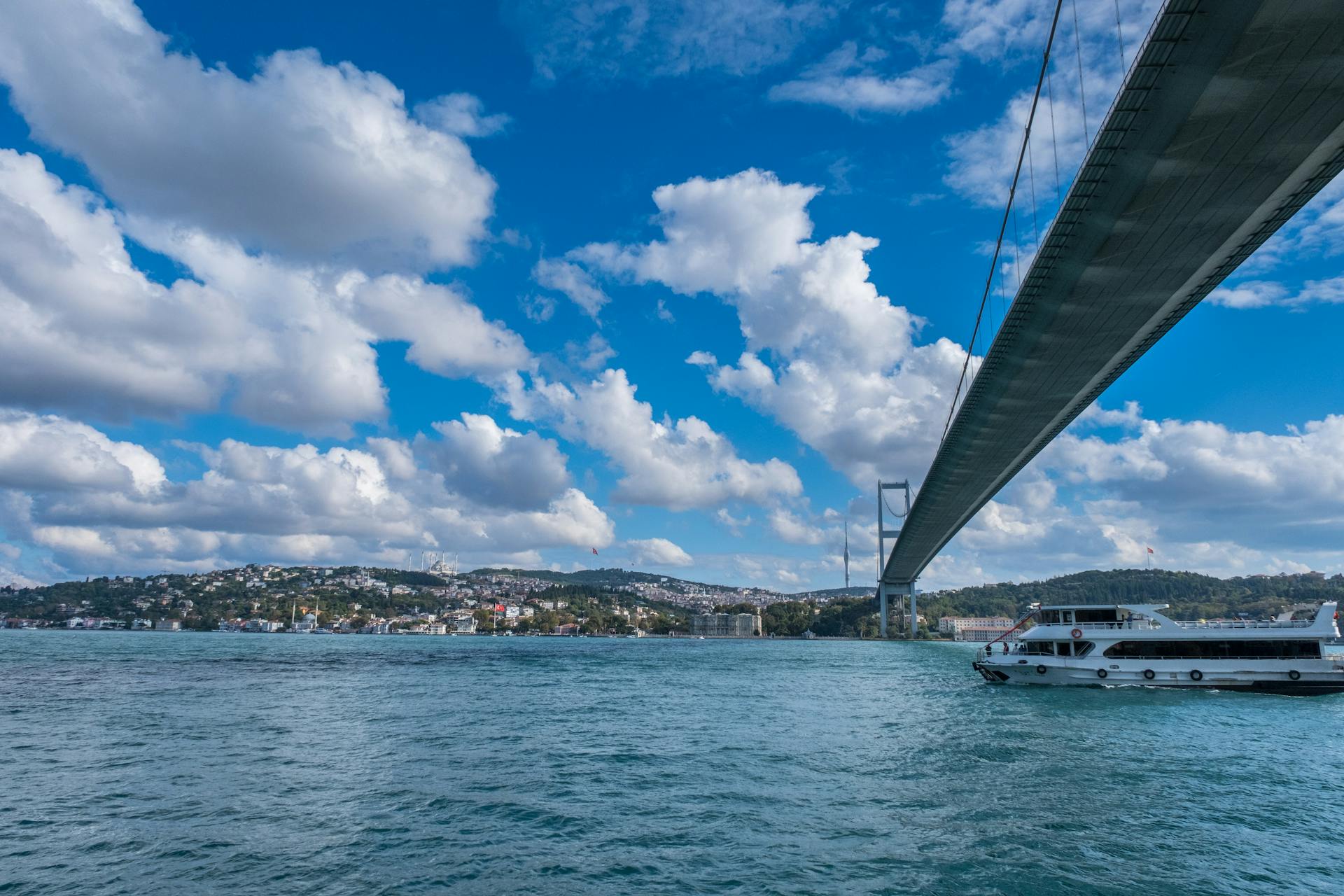 View of the Bosphorus Bridge and a ferry boat under a bright blue sky with clouds in Istanbul, Turkey.